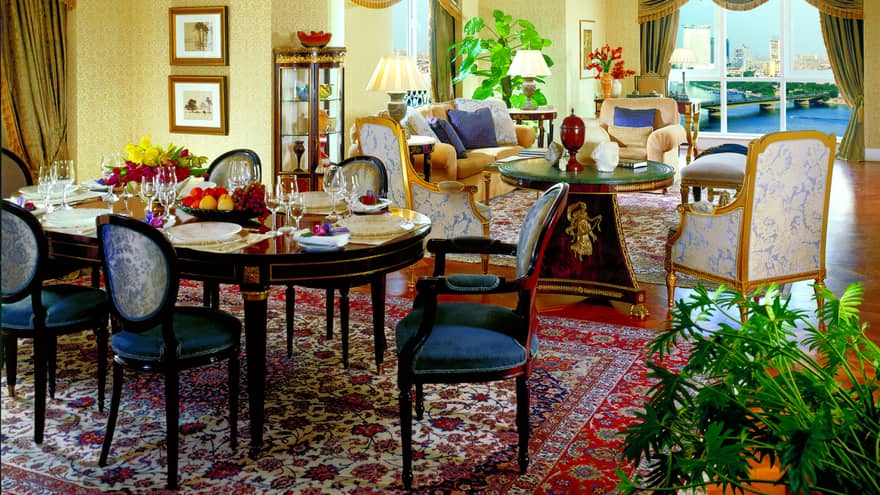 Dining table with formal service for 10, antique-style blue chairs, cafe table and armchairs in background
