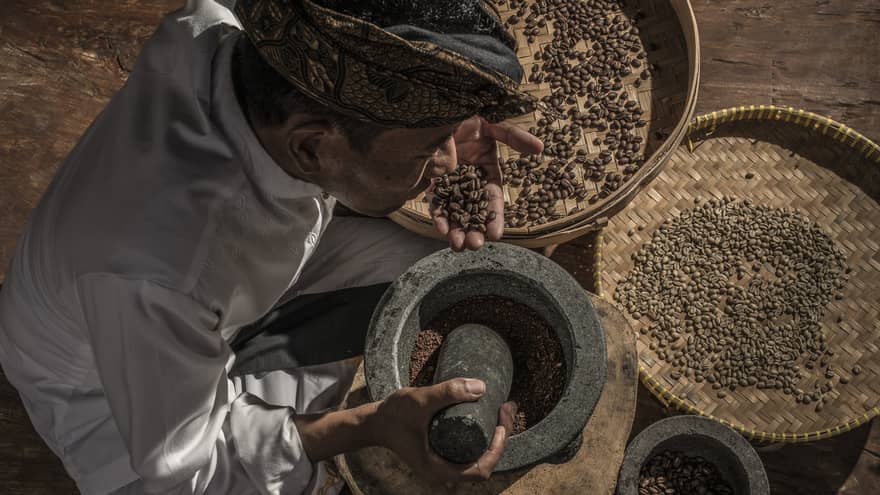 A coffee grower with coffee beans in a large mortar and pestle at Four Seasons Bali and Jimbaran Bay