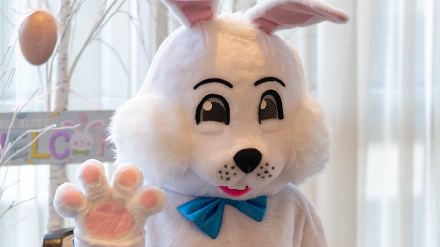 A person wearing an Easter Bunny costume and sitting near a tree decorated with Easter eggs