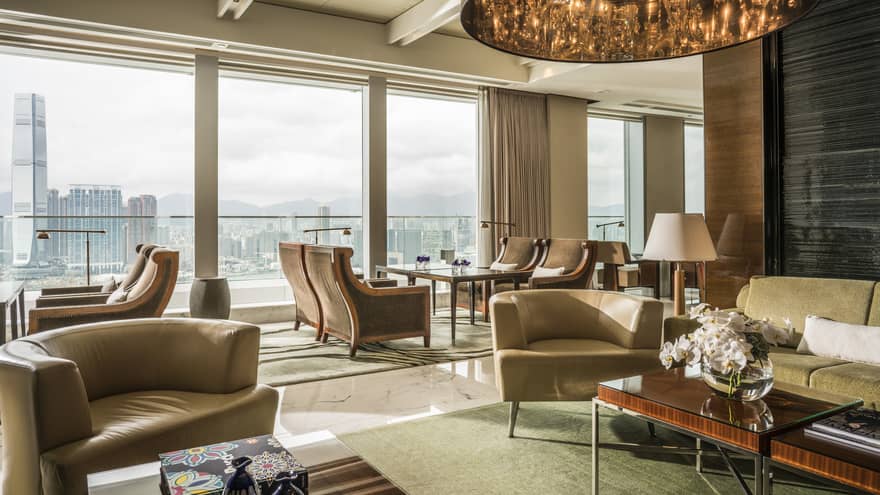 A spacious, modern lounge area with large windows offering a panoramic cityscape view. The room features comfortable armchairs, sofas, wooden furniture. 