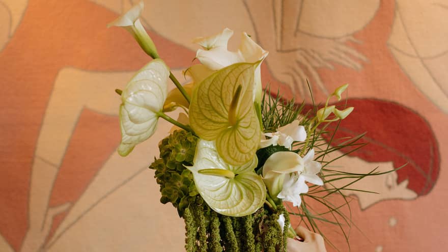 An extended arm hold a wedding bouquet made with white orchids and greenery in front of a pink-and-white mural