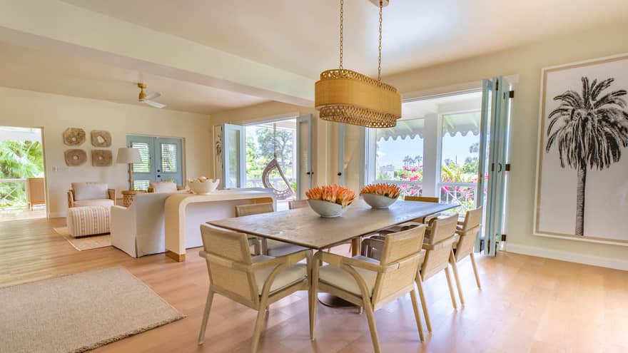 Dining room table with eight chairs, modern rattan lighting fixture, palm tree artwork, wooden floors and walk-out terrace