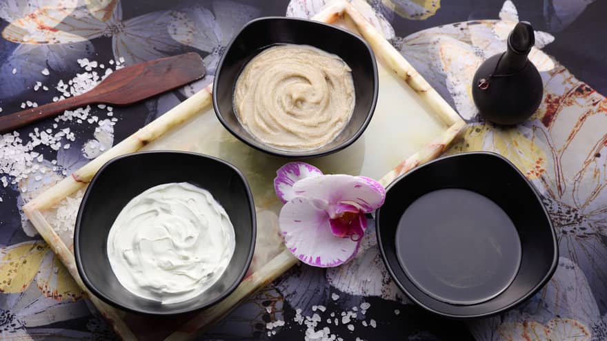 Looking down at three small black bowls with lotions, oils, fresh orchid flower