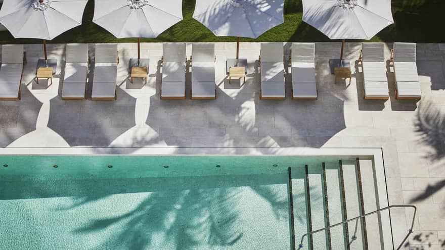 ,Elegant outdoor pool at Four Seasons Resort with sun loungers, white umbrellas, palm trees, and lush greenery, creating a serene and luxurious atmosphere.
