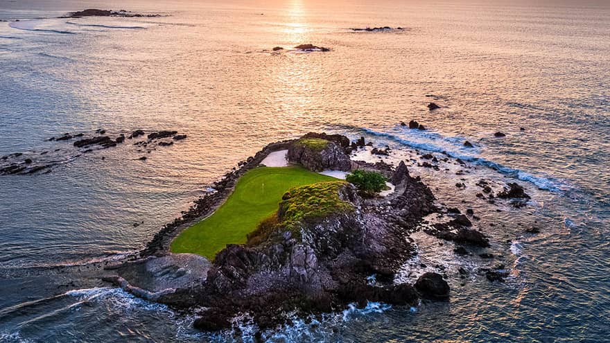 A small island that is part of a gold course, the sun is rising in the distance.