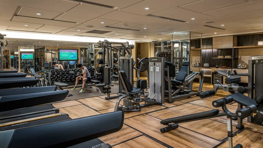 Man sits on bench, lifts weights on Fitness Centre by cardio machines 