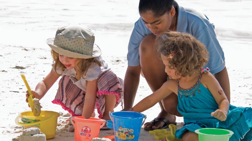 Kuda Velaa hotel staff helps young children with plastic buckets dig in sand on beach