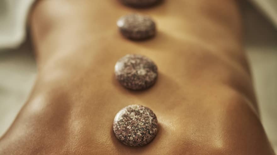 A woman lies on a spa table with four hot stones laid on her back
