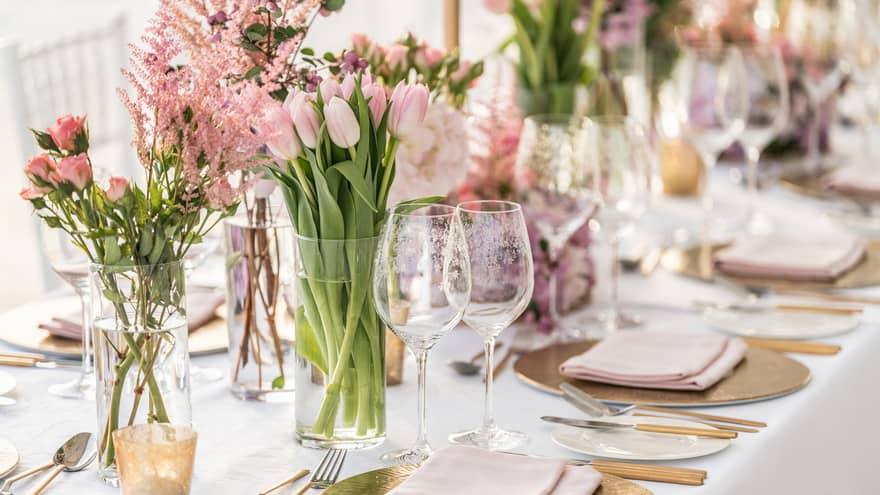 A banquet table is decorated with gold chargers, pale pink linens and a variety of pink florals