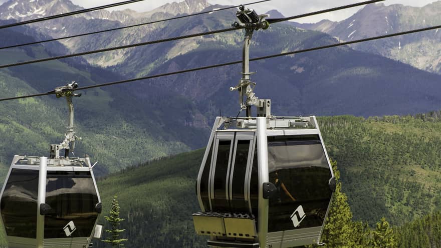 Two gondolas travelling over a forested area.