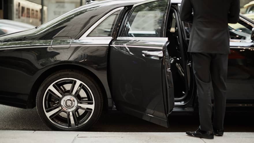Man in suit by open door of black luxury car