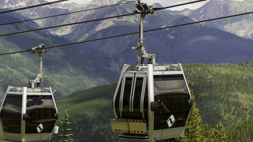 Two gondolas travelling over a forested area.
