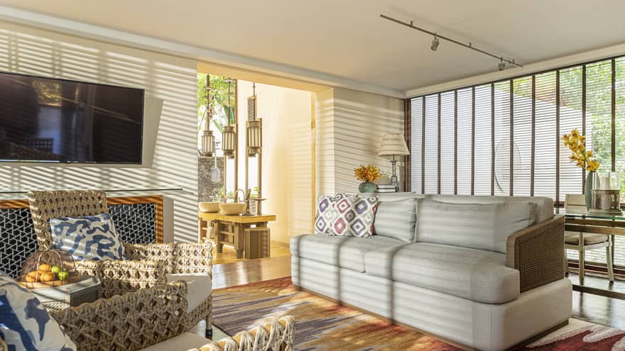 The sun streams into a living room through wooden window shutters