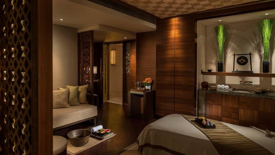 Spa treatment room with carved wood detail walls, bed and table with trays with oils