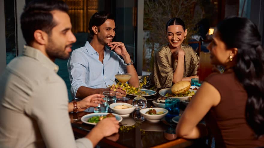A group of four people sit smiling around a restaurant table filled with food