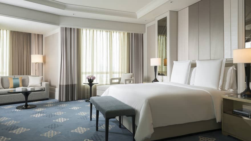Spacious hotel room with blue pattern carpet, king sized bed and white bedding