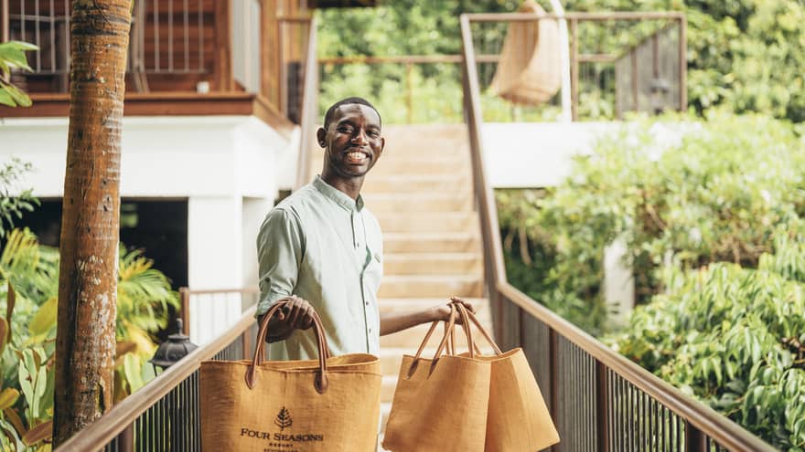 Person in linen shirt standing on catwalk holding four orange tote bags