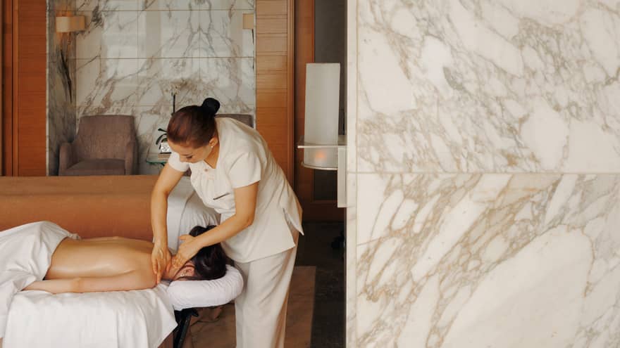 A female spa therapist performing a massage on a woman, face down on spa treatment table, in a chic luxury spa with marble walls