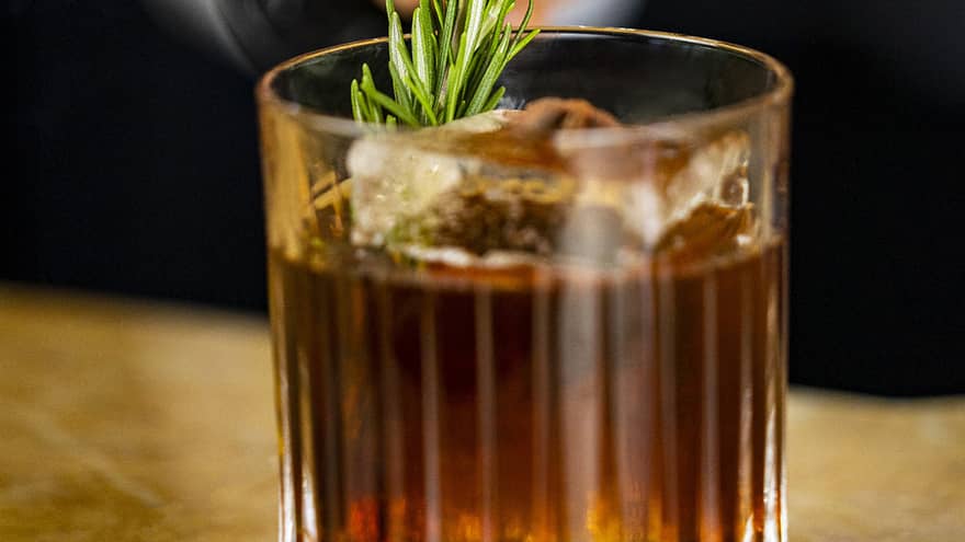 A dark amber coloured cocktail with an herb garnish.