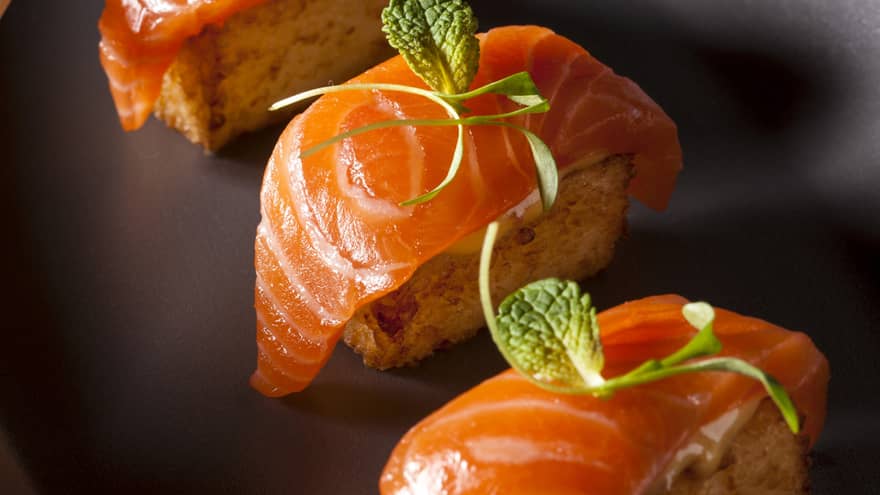 Three pieces of crispy salmon sushi on black platter