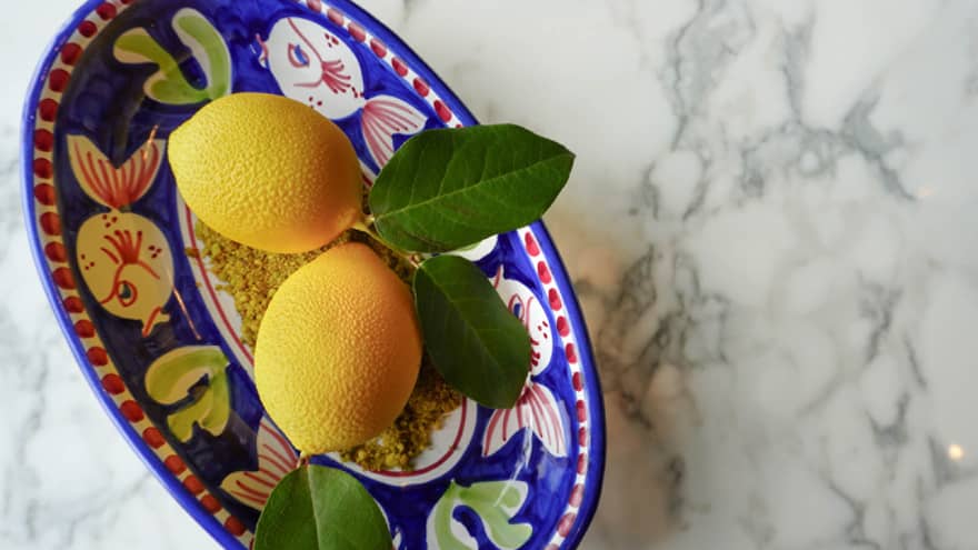 Lemons in a blue bowl with yellow and white fish painted on it.