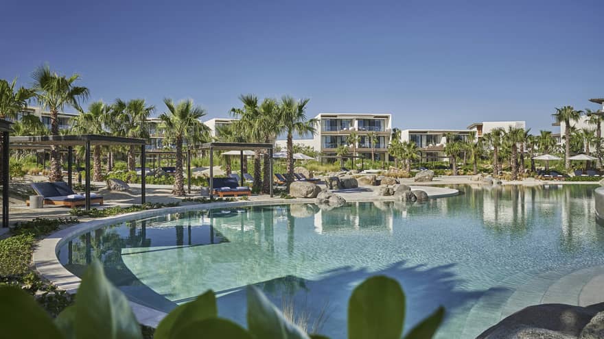 A large round pool surrounded by palm trees, grass, and a hotel.