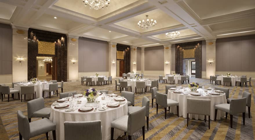 Several round tables set with white table clothes and square chairs.