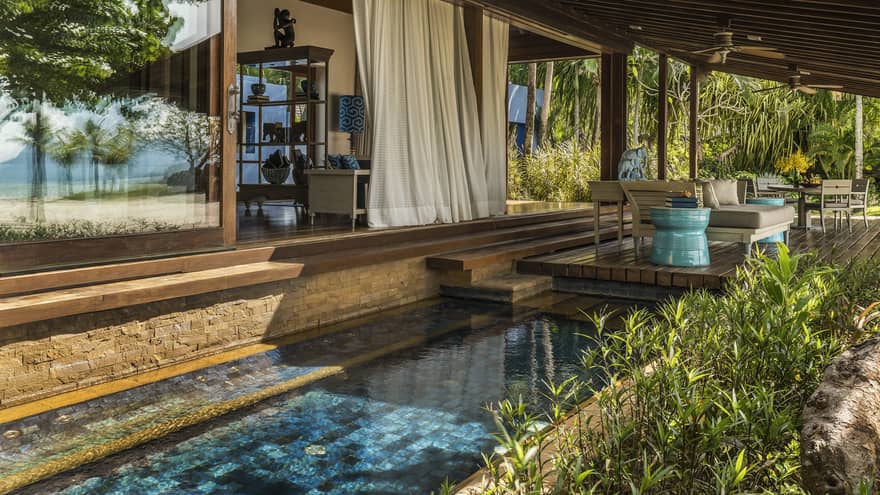 A private plunge pool built into an expansive patio surrounded by lush greenery. 