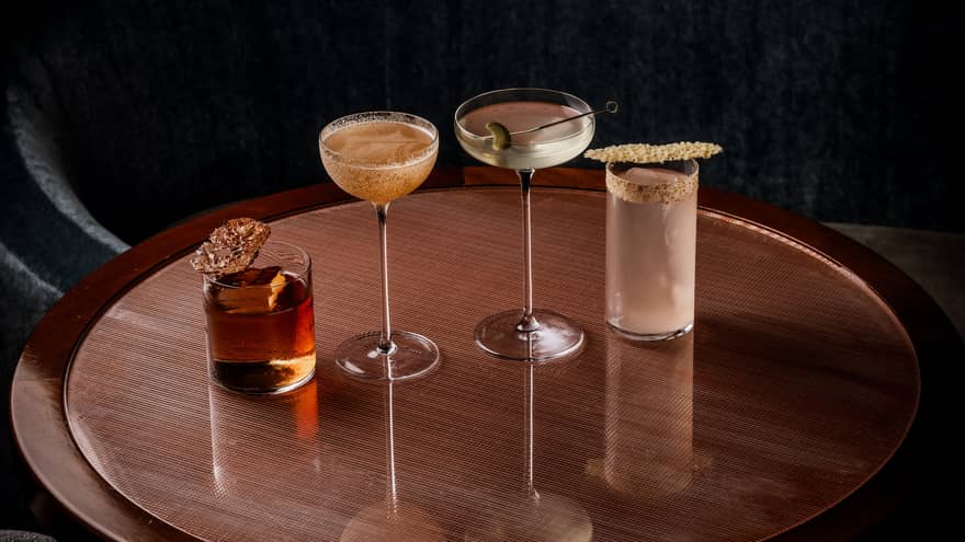 Four cocktails each in a different style of glass are set in a row on a round wooden table