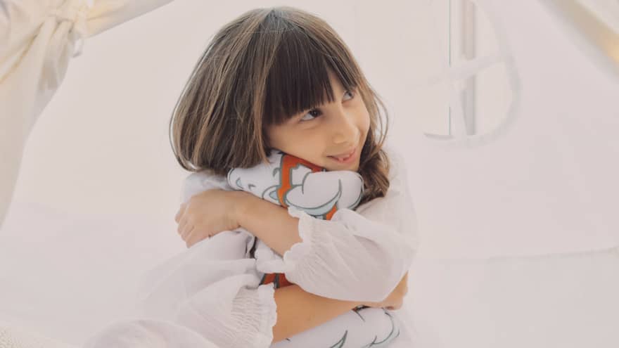 A child dressed in white holds a stuffed animal as she sits in a play tent in a guest room.