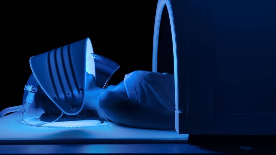 Person wears mask with blue lights under dome in dark spa room