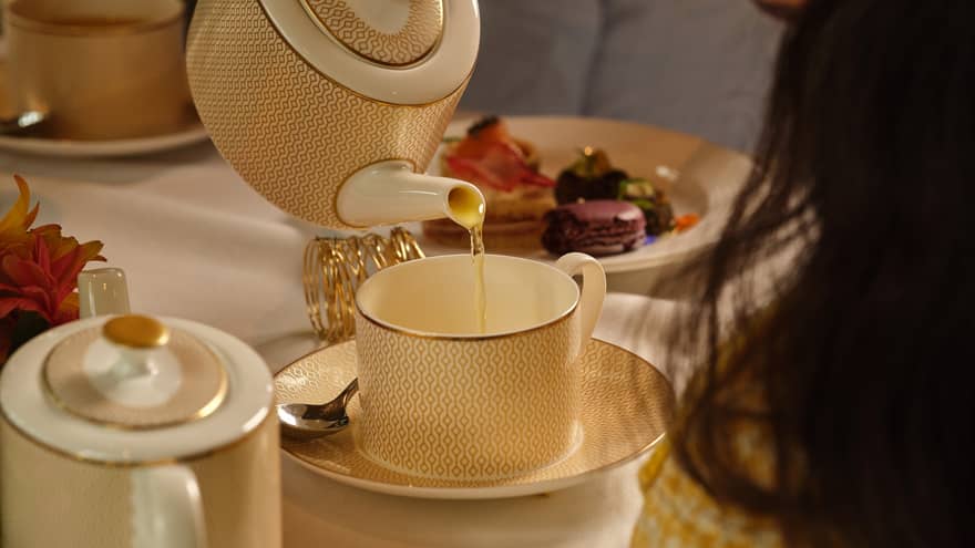 Person pours tea from a cream porcelain tea pot into a matching mug