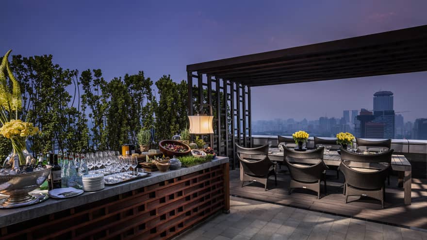 A rooftop terrace with dining and bar areas overlooking the city skyline. 