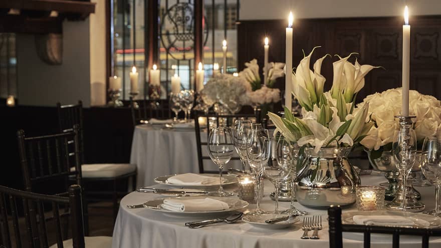 A white linen table illuminated by candlelight, and decorated with peace lilies.
