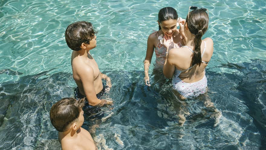 Four children stand in a pool that glistens from the sunshine