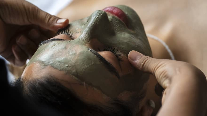 A person lying supine on a spa treatment table receives a facial treatment.