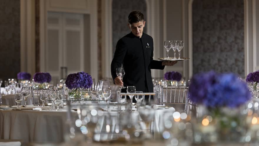 Hotel staff sets empty wine glasses on banquet dining table in ballroom