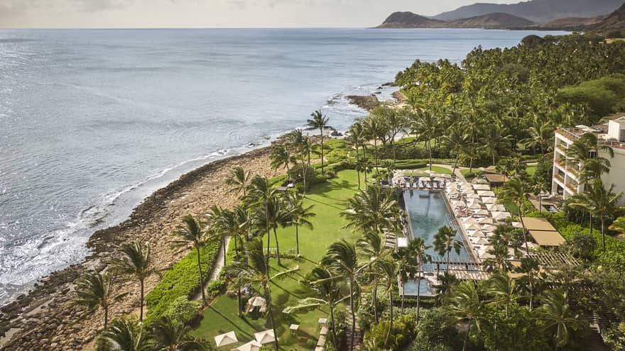 Tropical Hawaiian resort featuring a green lawn and pool, next to the beach
