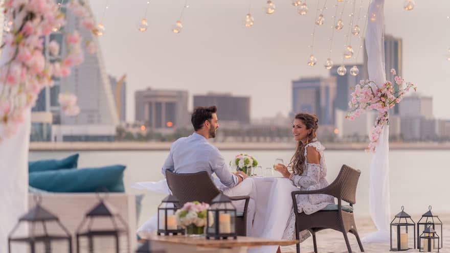 A man and woman enjoy a romantic dinner outside by the water overlooking the city