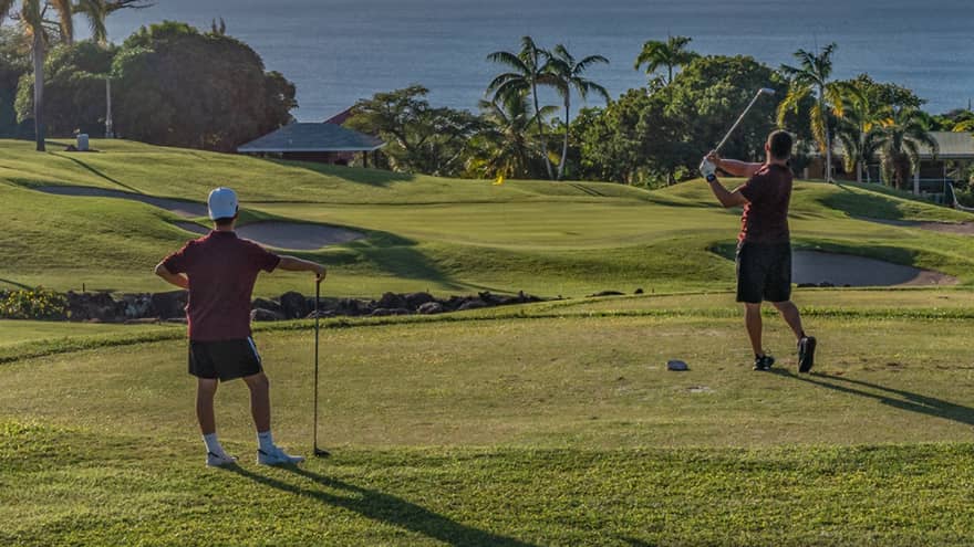 Two guests on a golf course near the ocean swinging golf clubs