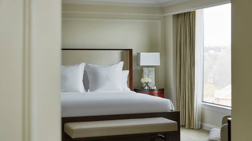 Presidential Suite west wing bed with white linens, white bench, sunny window through door frame