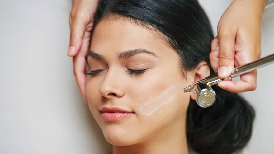 Close-up of woman's face with eyes closed as spa staff holding an airbrush administers Intraceuticals therapy