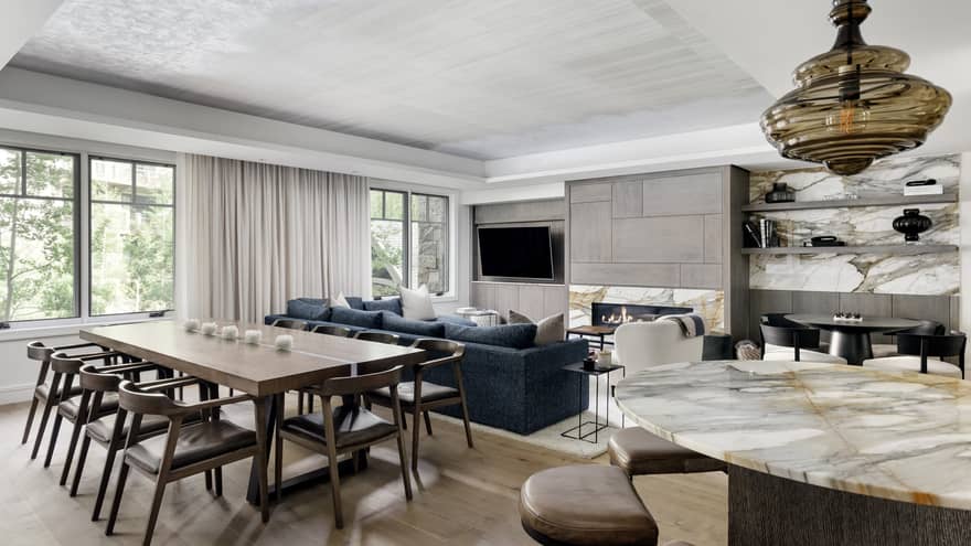 Contemporary, light-filled hotel residence featuring a marble dining table, a rectangular, wooden, formal dining table, and a living room with a stone hearth