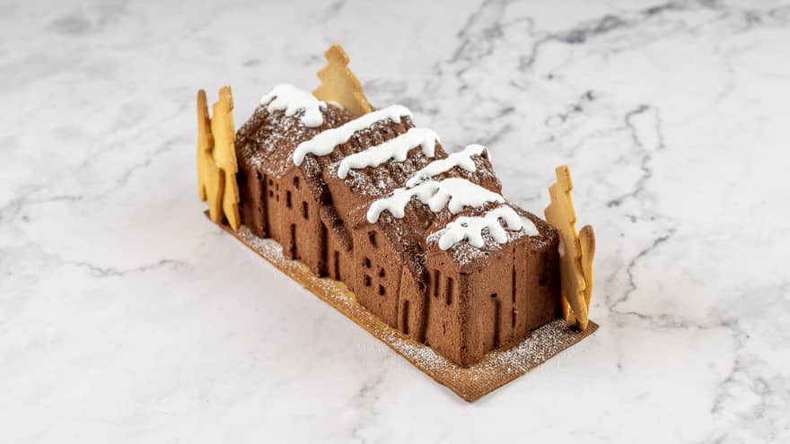 Yule log shaped to look like a small village with cookies as trees and white frosting on top