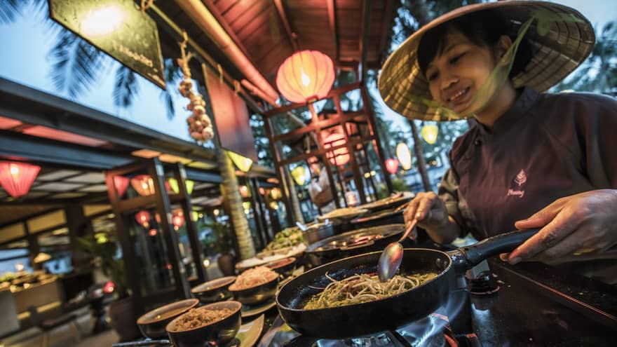 Chef cooks street food noodles in traditional Vietnamese rice hat