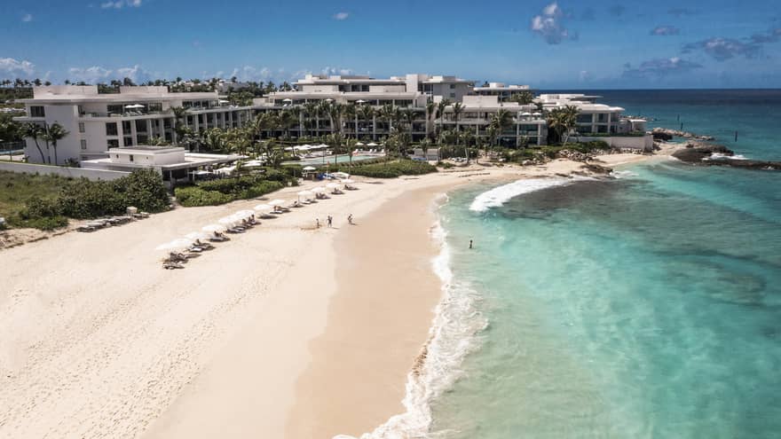 Aerial view of beachfront resort with row of chairs and umbrellas on the sand and turqouise water lapping up on the shore