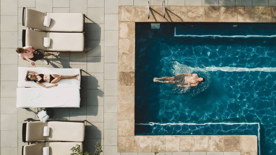 Woman laying in pool chair while man swims in pool.