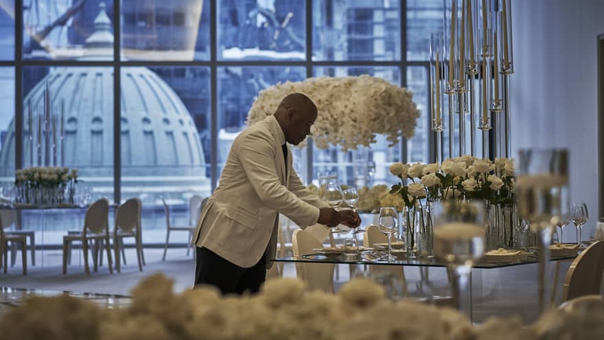A four seasons staff does the finishing touches on a circular table in the ballroom, decorated with extravagant white florals