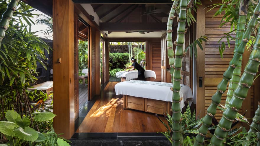 Spa staff spreads sheet on couples massage beds on open-air pavilion 