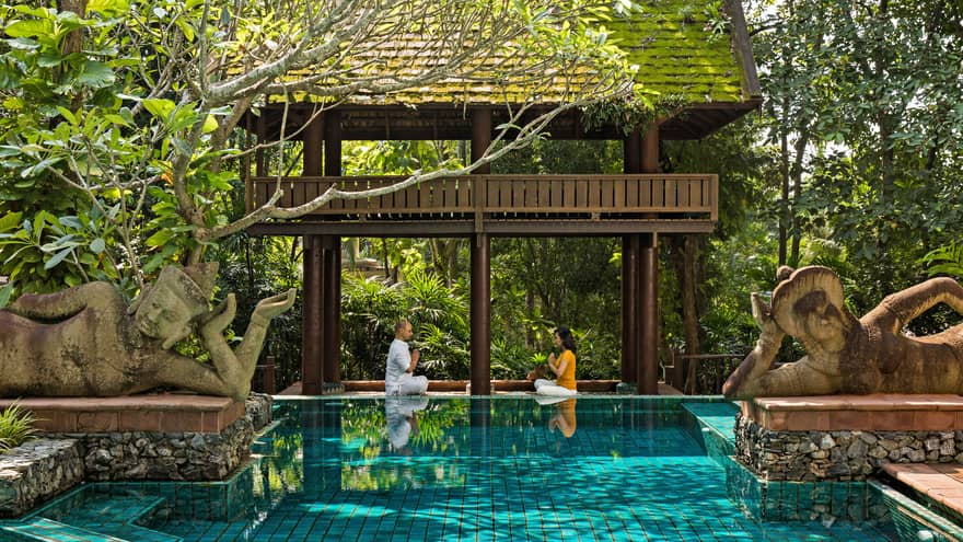 Couple practicing meditation in an outdoor pool setting 